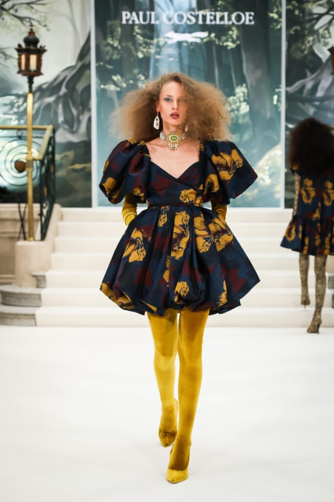 Model walking for Paul Costelloe AW22 London Fashion Week Show wearing mustard tights paired with a floral mini dress