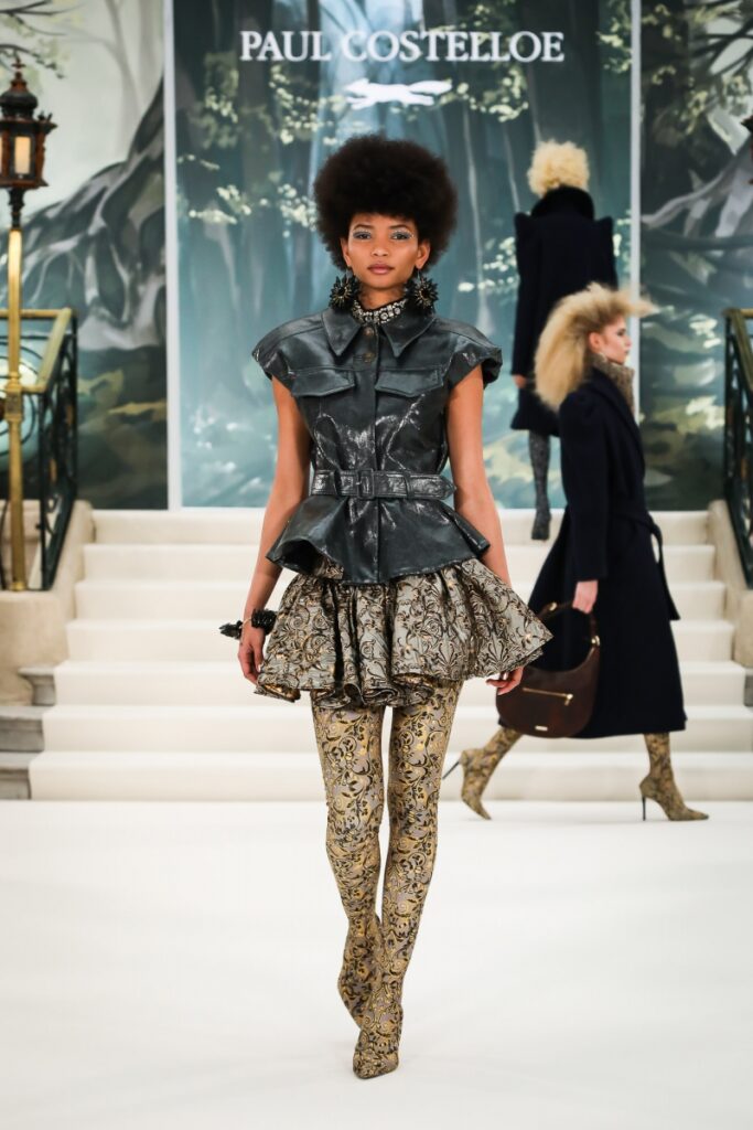 Model walking for Paul Costelloe London Fashion Week show, wearing leather tunic and brocade boot legging hybrid 
