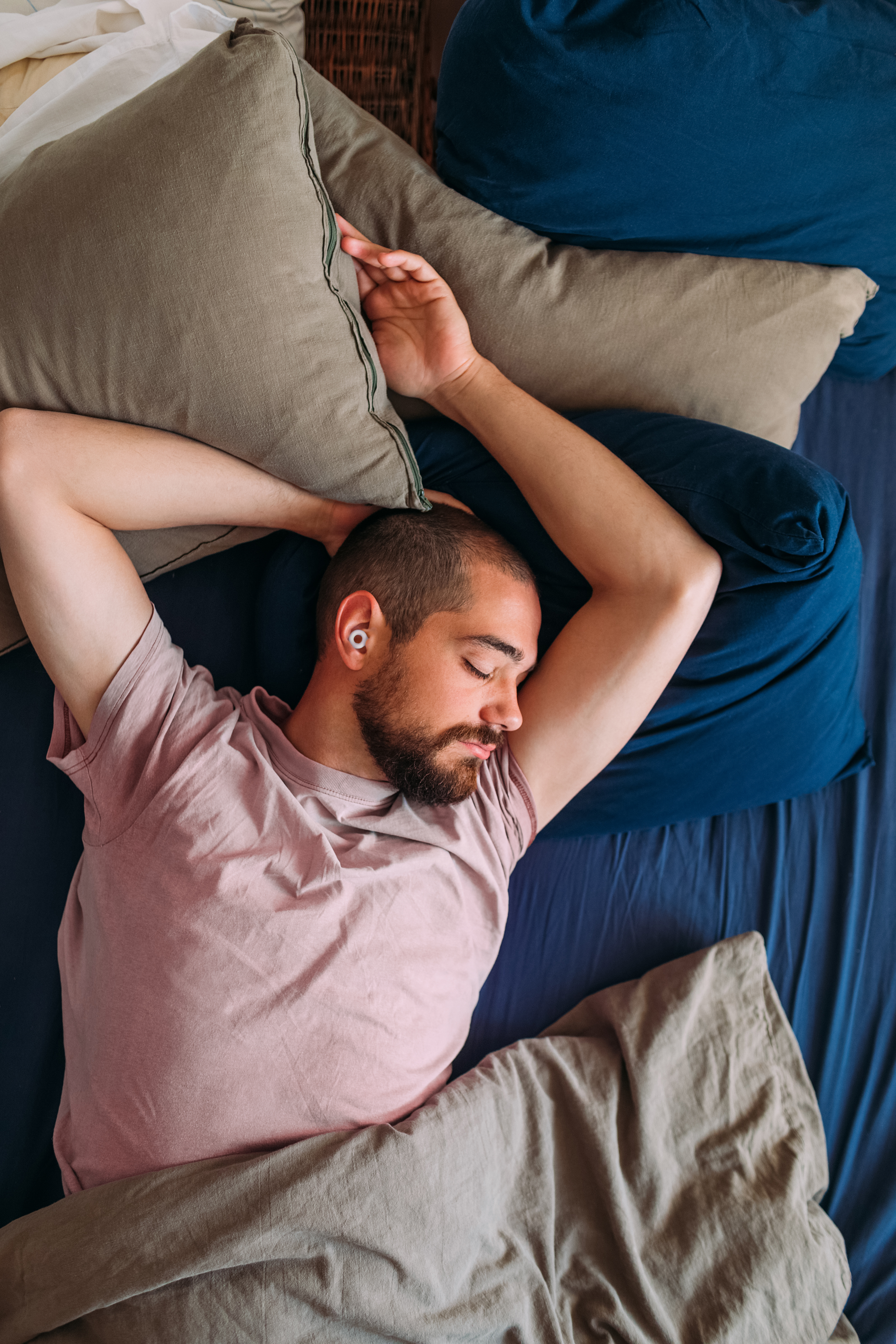 A man sleeping with one arm up, with an earplug in 