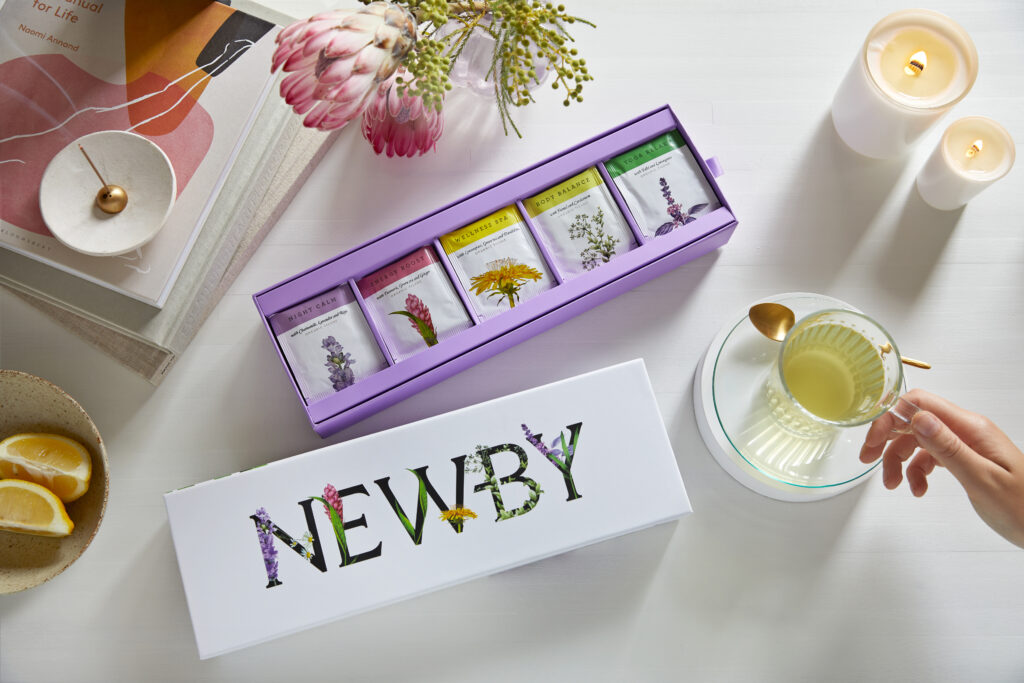 Newby Teas Wellness collection surrounded by candles, flowers and a cup of tea.