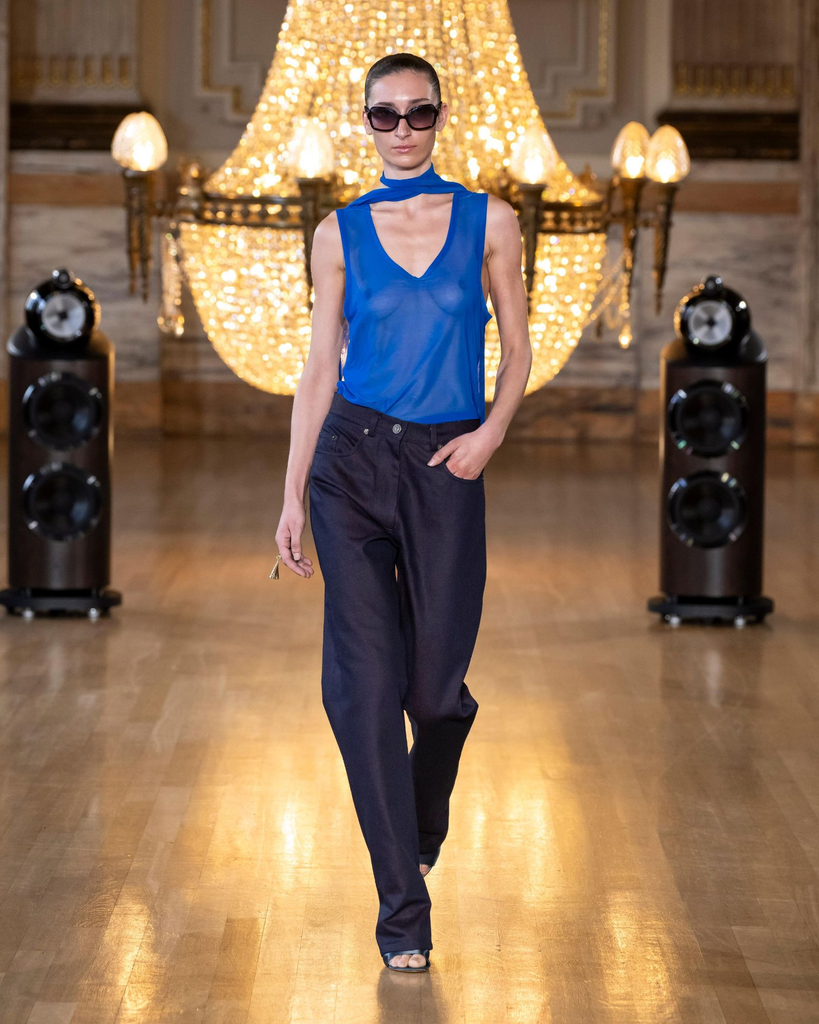 Caucasian female model with sunglasses, light blue see-through blouse, dark blue denim jeans, and open-toes sandals, at Labrum SS27 Runway